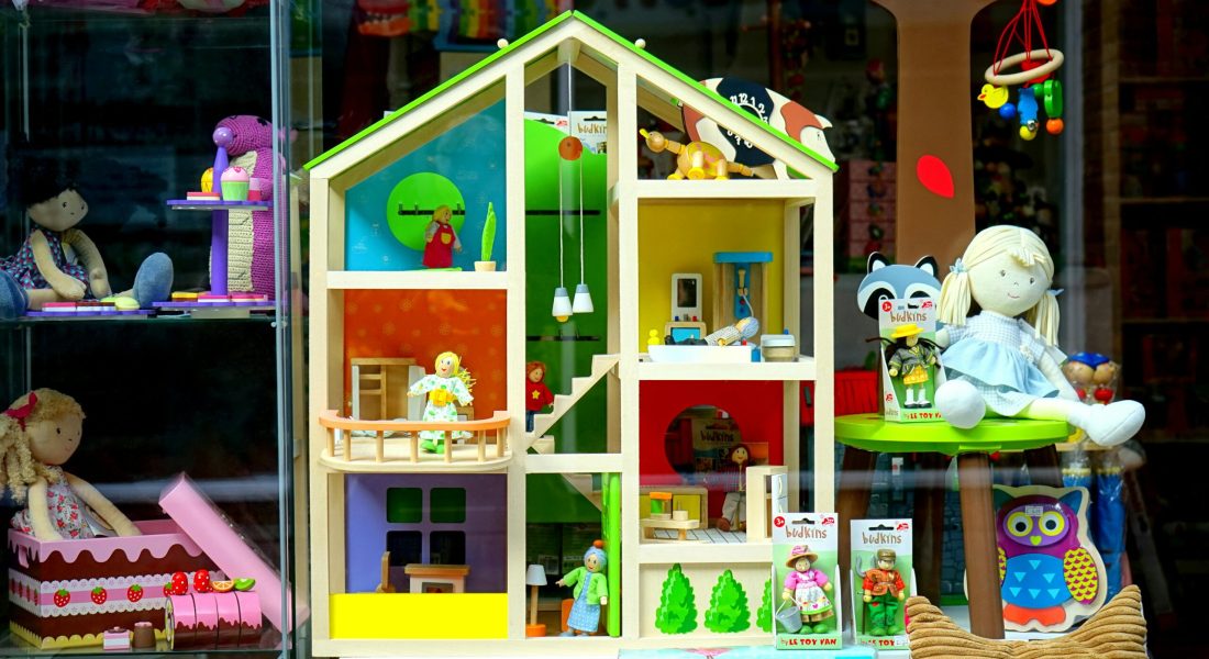 A vibrant dollhouse and stuffed toys displayed in a toy store window, perfect for children's play.